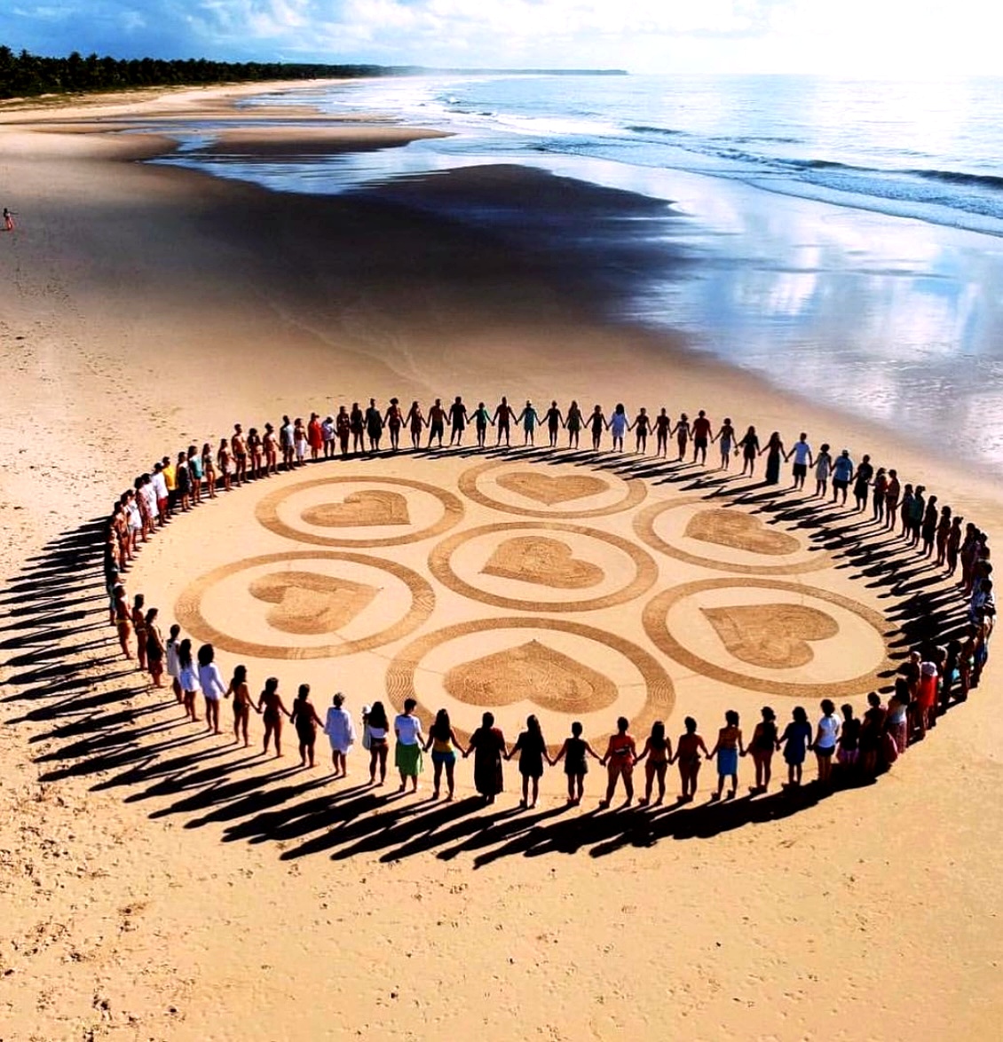 Human mandala on Piracanga beach, Brazil — community holding hands in a circle around a sand mandala